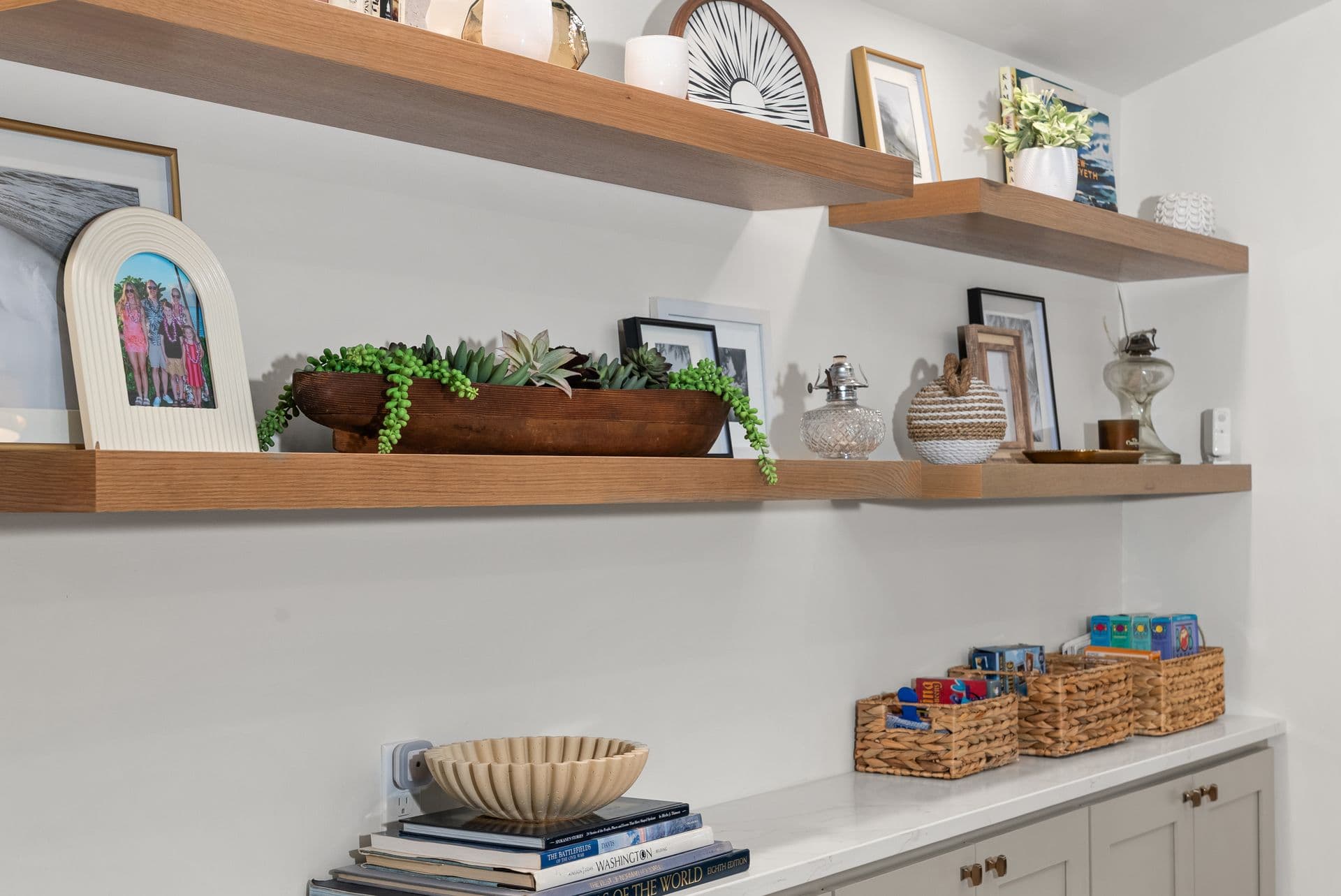 Built-in wooden shelves displaying framed photos, decorative items, potted succulents, and woven baskets above a white cabinet.